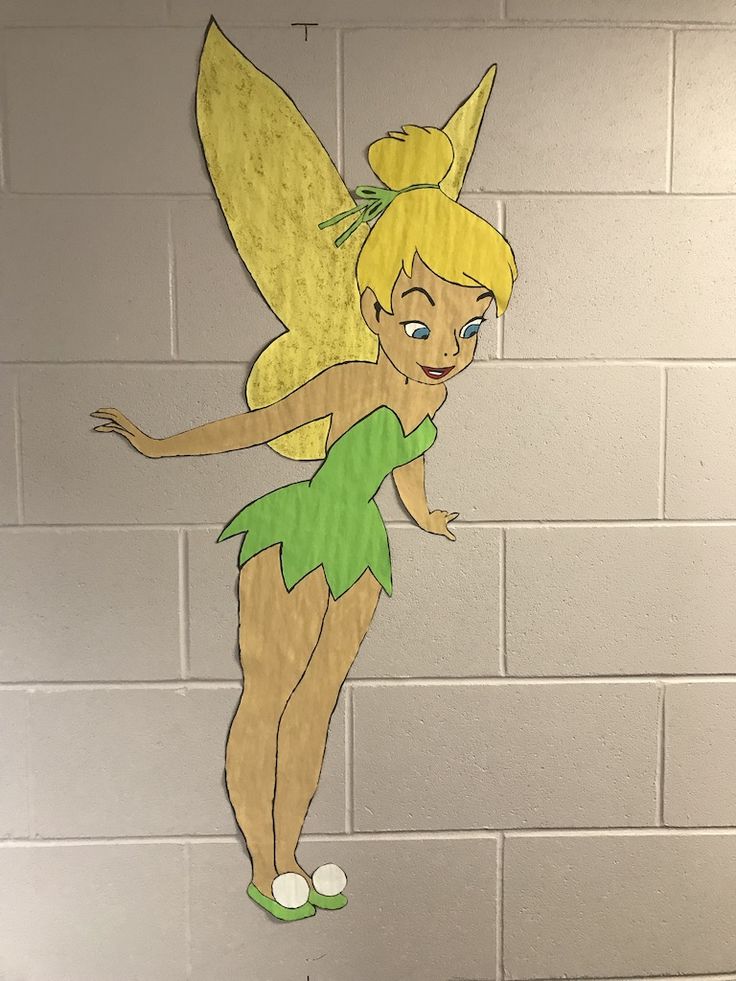 a paper cut out of tinkerbell standing in front of a white brick wall