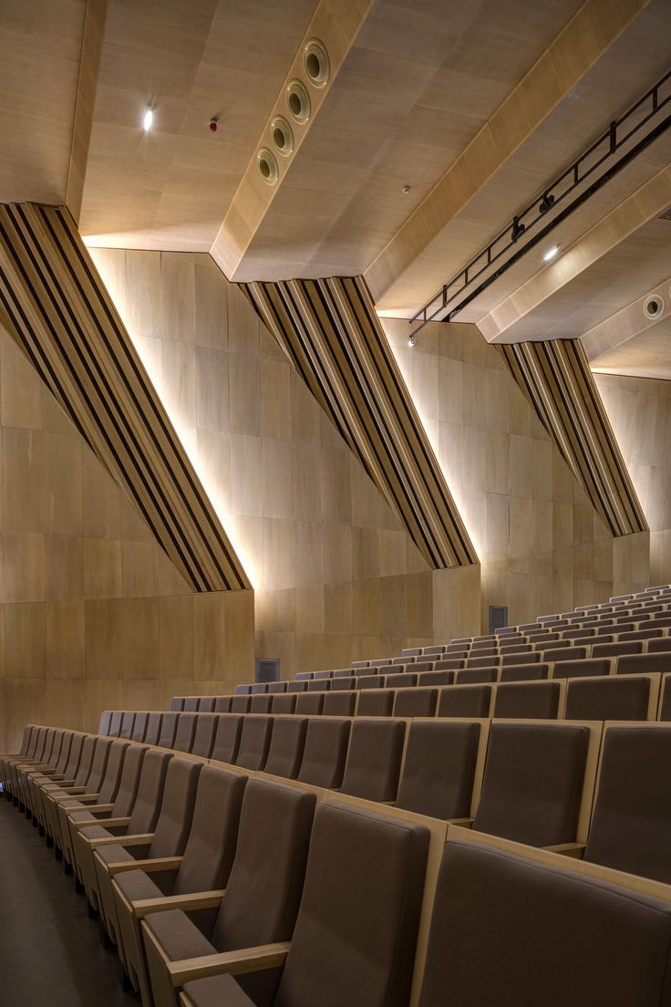 an empty auditorium with rows of seats in front of the wall and ceiling lights on either side