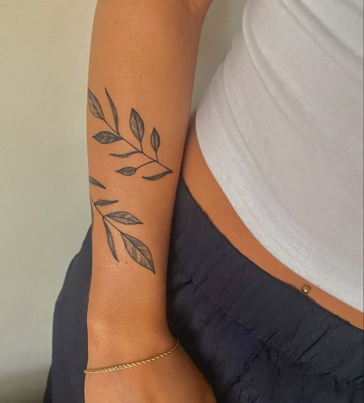 a woman's arm with leaves on it and a gold chain around her wrist