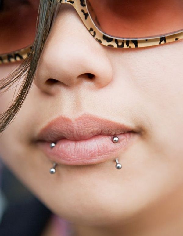 a close up of a person wearing sunglasses and piercings on her nose, with one eye partially closed