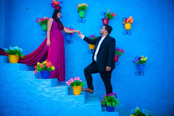 a man and woman standing on some steps with flowers in the pots next to them