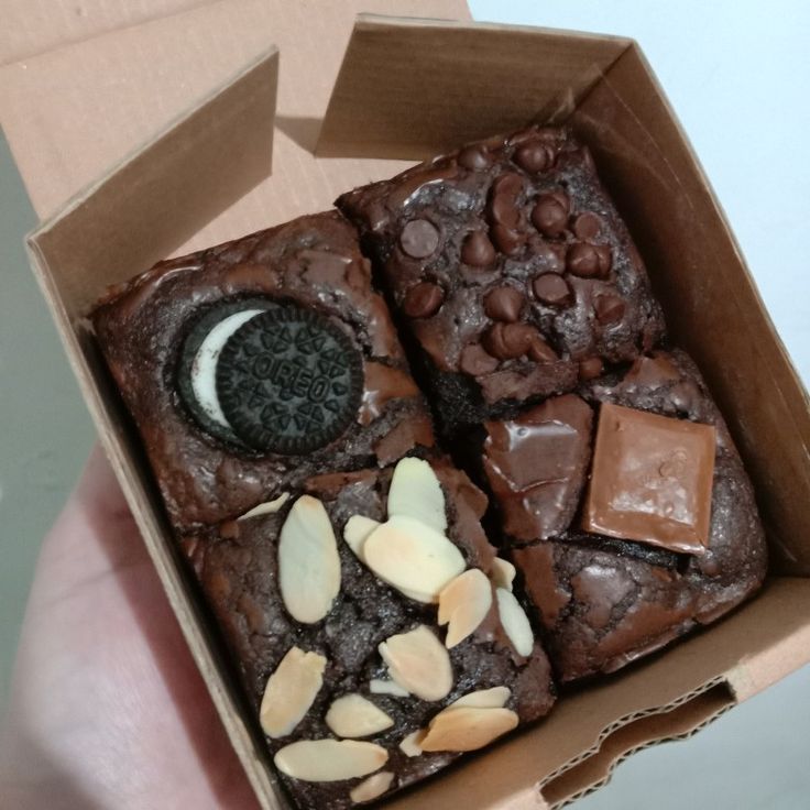 a box filled with brownies covered in cookies and chocolates next to a person's hand