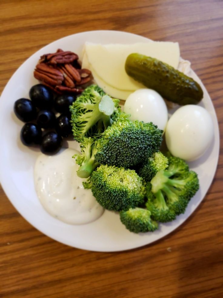 a white plate topped with broccoli, eggs and other foods on top of a wooden table