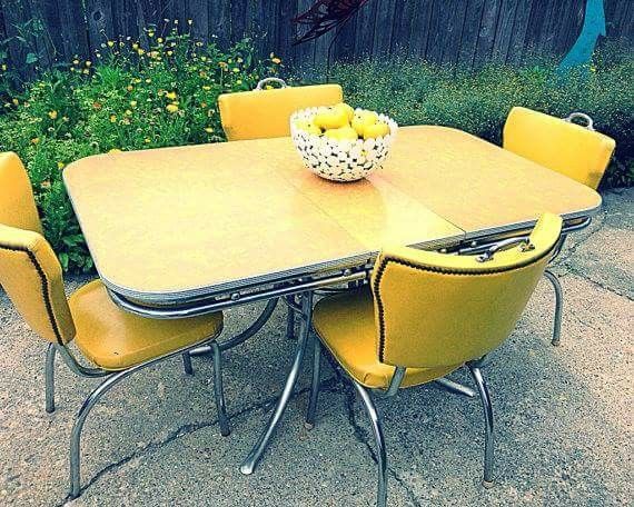 a table with yellow chairs and a bowl of lemons on it in front of a fence