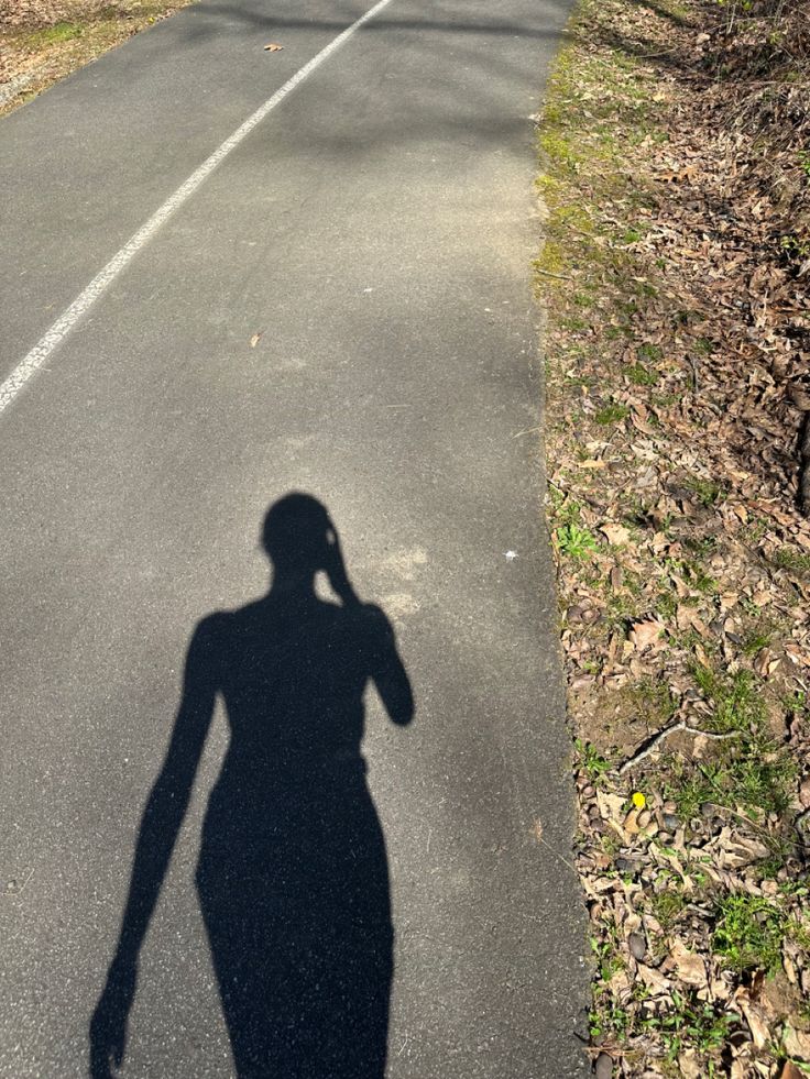 the shadow of a person walking down a road with a cell phone to their ear