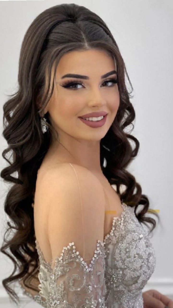 a woman with long dark hair wearing a white dress and diamond earrings smiling at the camera