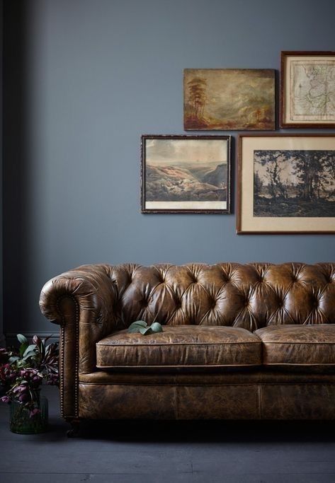 a brown leather couch sitting in front of two pictures on the wall next to a vase with flowers