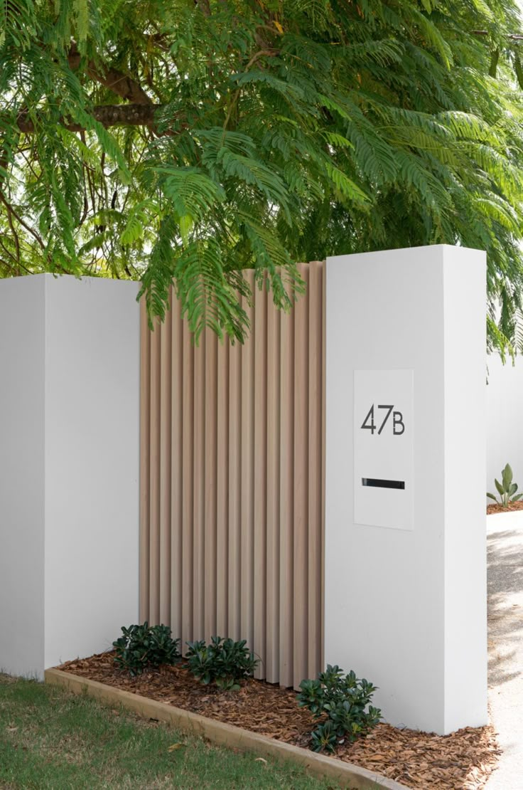 a white wall with a wooden fence next to it and some plants on the ground