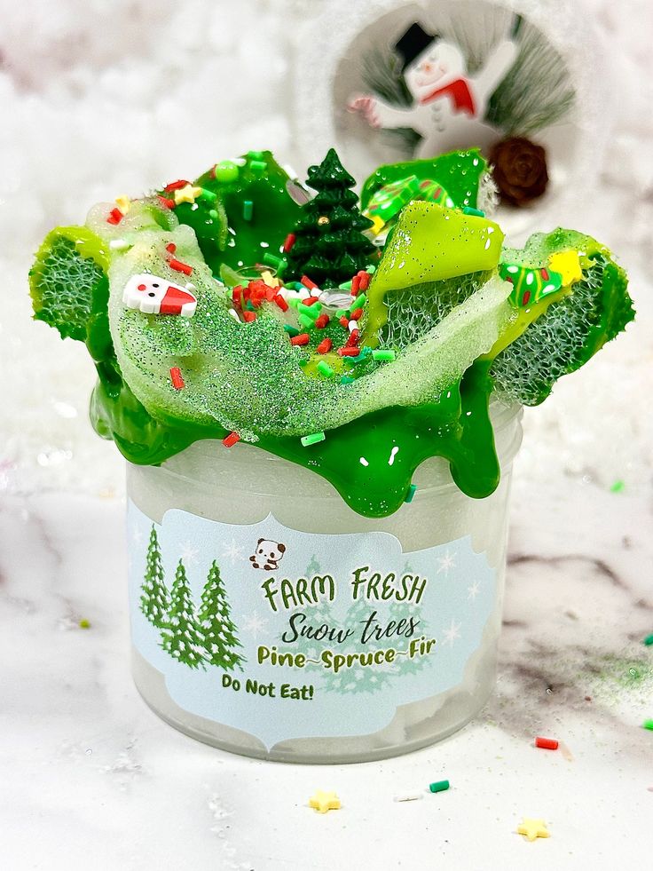 a glass jar filled with green and white frosted christmas decorations on top of snow covered ground