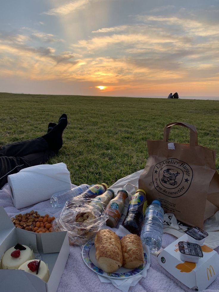 a picnic table with food and drinks on it in the middle of a grassy field