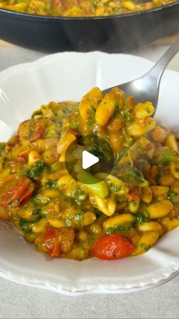 a white bowl filled with pasta and vegetables on top of a table next to a skillet