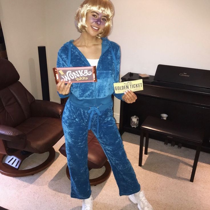 a woman in blue pajamas holding a bar of chocolate and smiling at the camera while standing next to a piano