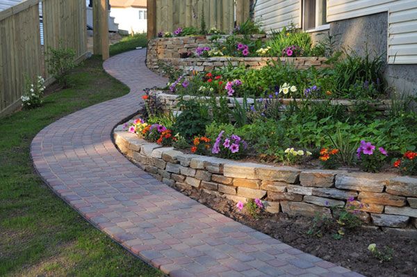 an outdoor garden with flowers and plants growing on the side of the house in front of it