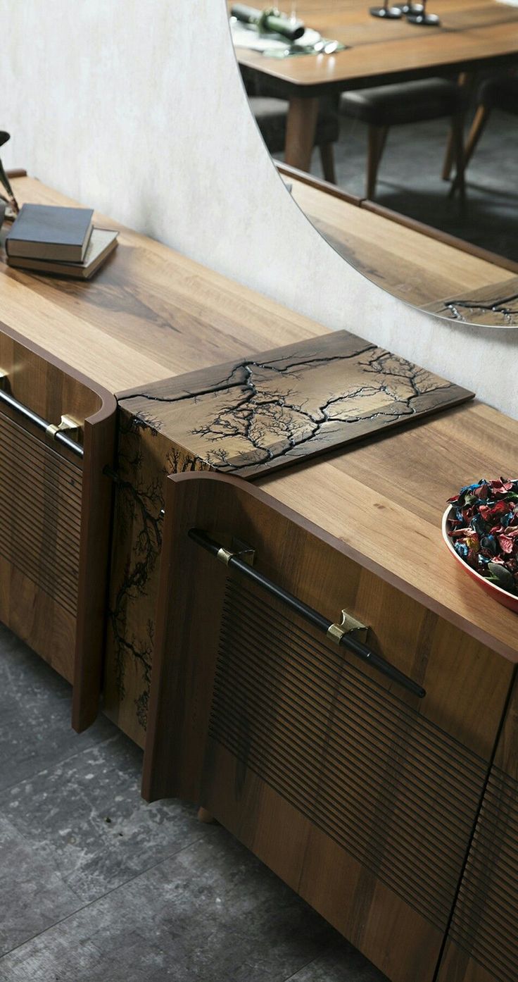 a bowl of fruit sitting on top of a wooden counter next to a mirror and table