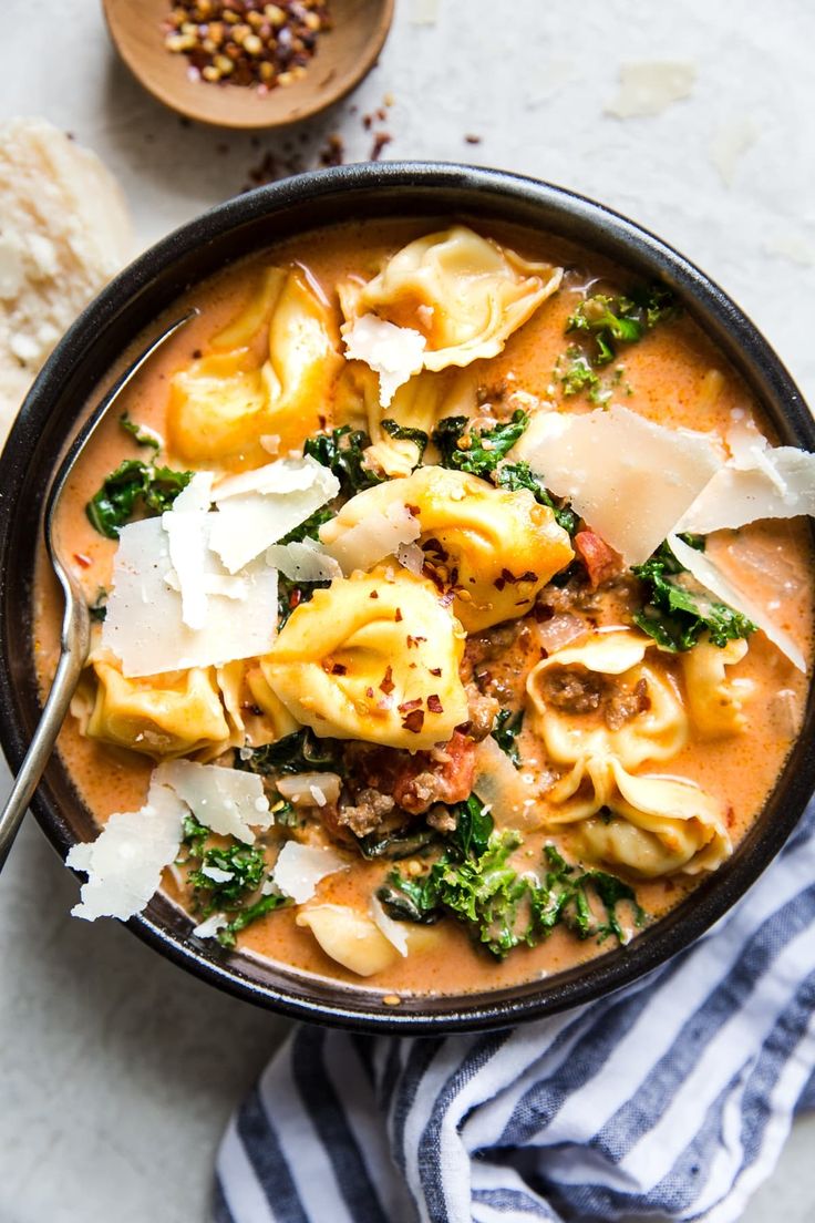 a bowl of pasta and spinach soup with bread on the side