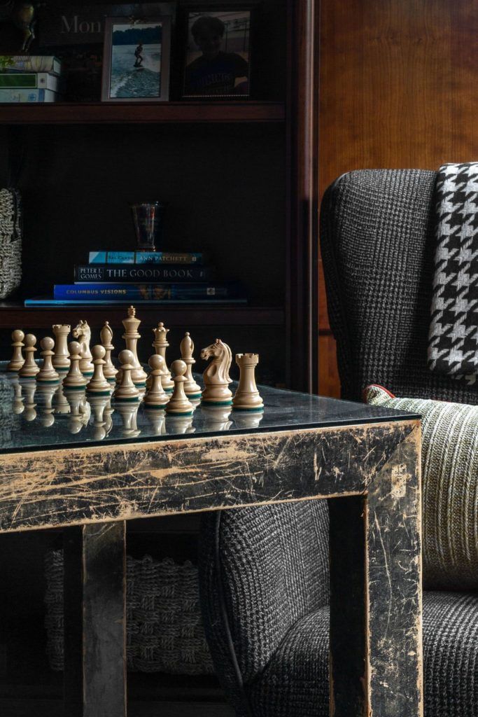 a chess set sitting on top of a wooden table next to a gray chair and bookshelf