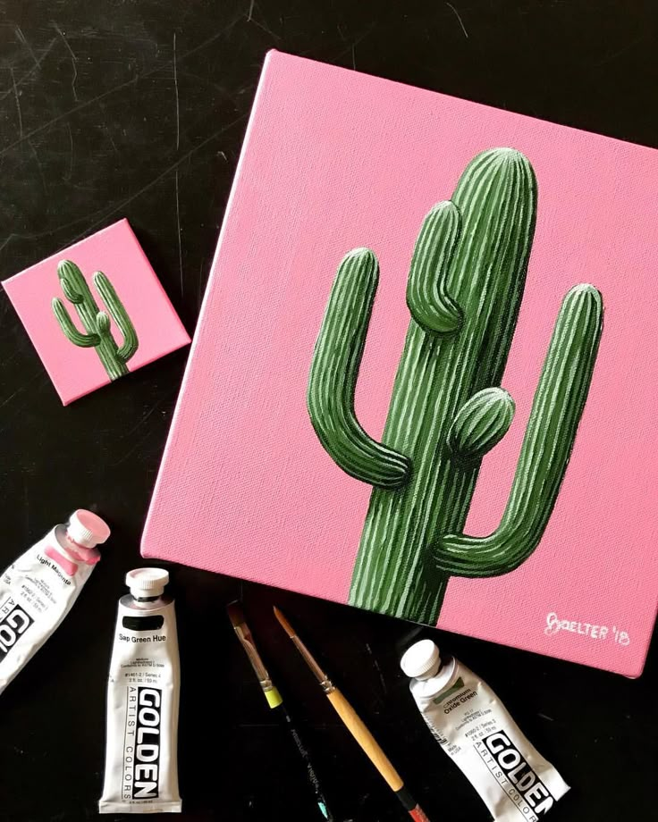 a painting of a green cactus on a pink background next to other paints and supplies