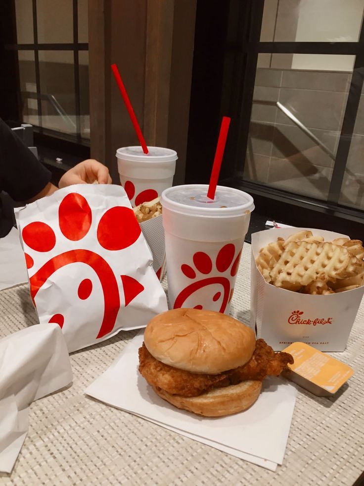 a chicken sandwich and waffle fries are on the table next to two cups of soda