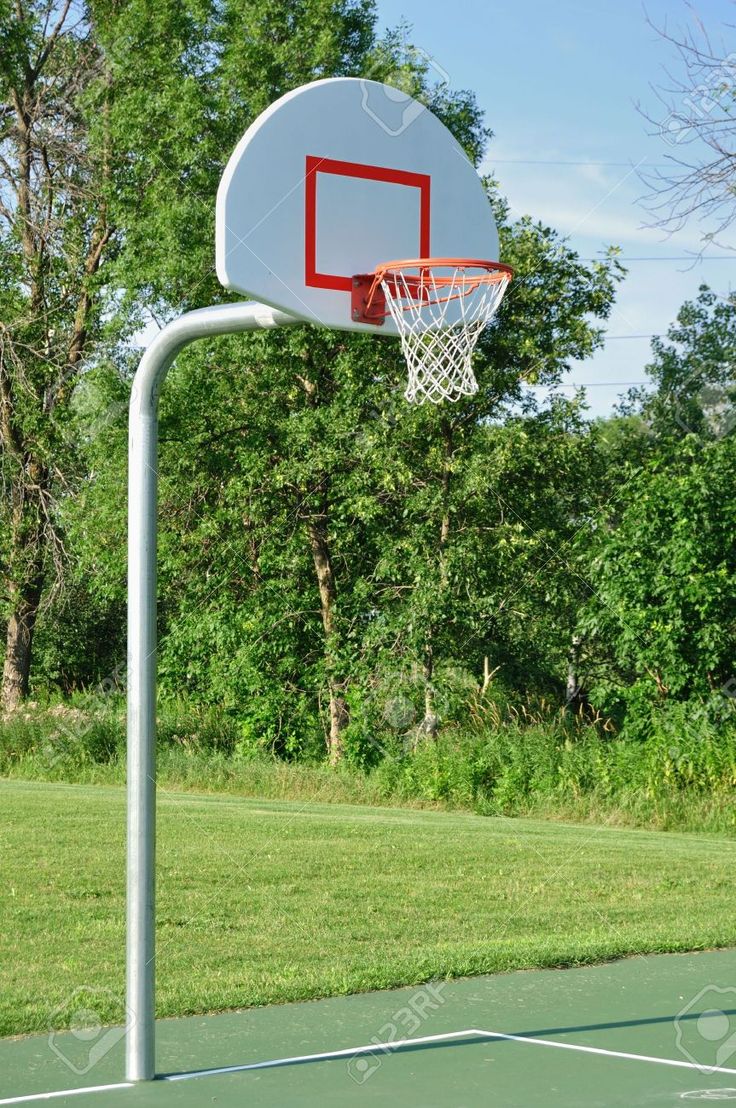 an empty basketball hoop in the middle of a field with trees and grass behind it