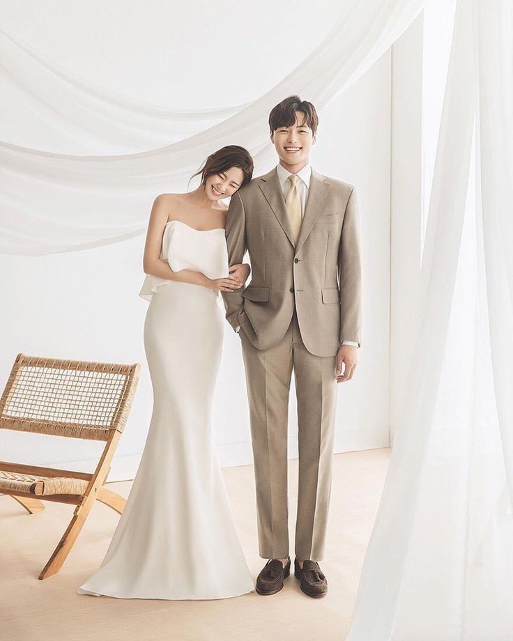 a man and woman standing next to each other in front of a white curtained room