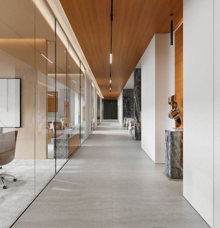 a long hallway with glass walls leading to an office area and desks on either side