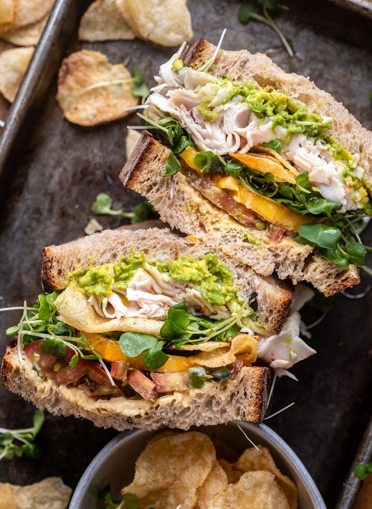 two halves of a sandwich sitting on top of a pan filled with potato chips and guacamole