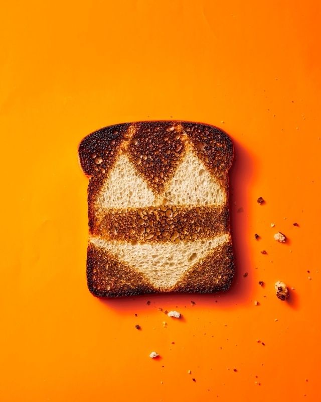 a piece of bread with white and brown toppings on an orange background, next to some seeds