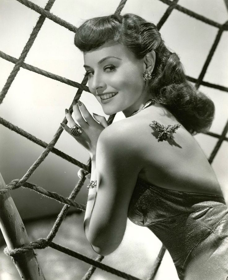 an old photo of a woman with tattoos on her arm and chest, leaning against a net