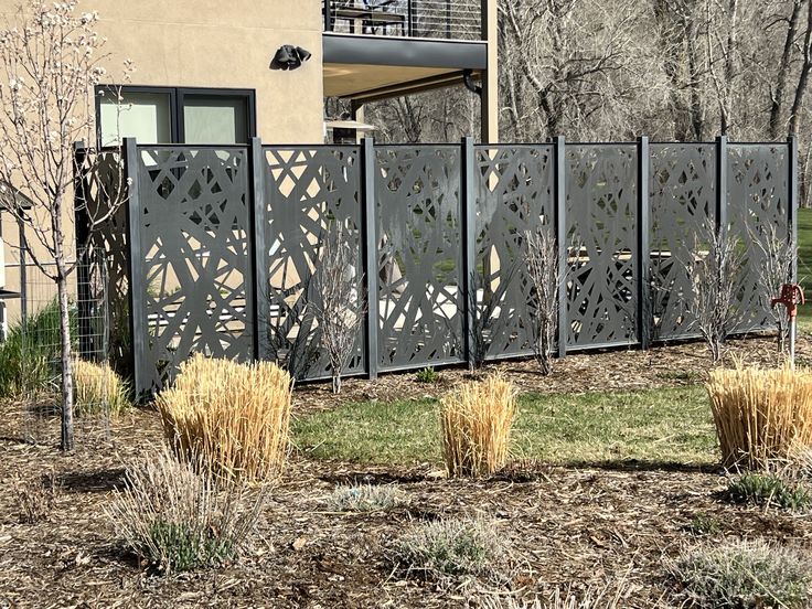 a large metal fence in front of a building with grass and bushes around it on the ground