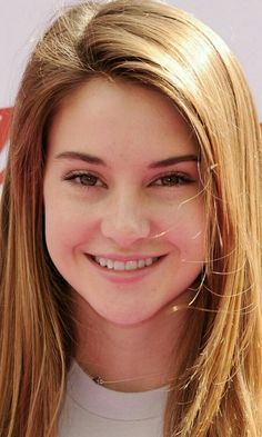 a close up of a person with long blonde hair and wearing a white shirt smiling at the camera