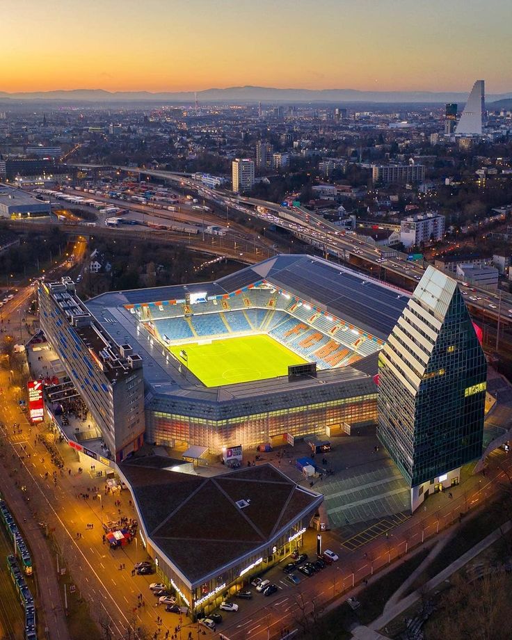 an aerial view of a soccer stadium at dusk with the sun setting in the background