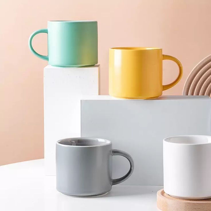 three different colored coffee mugs sitting on top of a white table next to each other