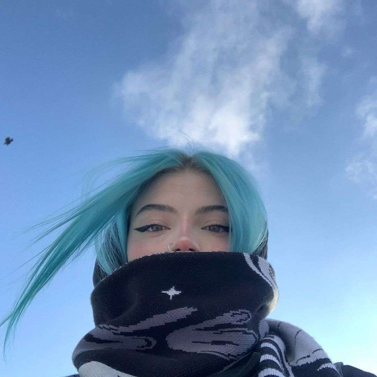 a woman with blue hair wearing a black and white striped scarf under a cloudy sky