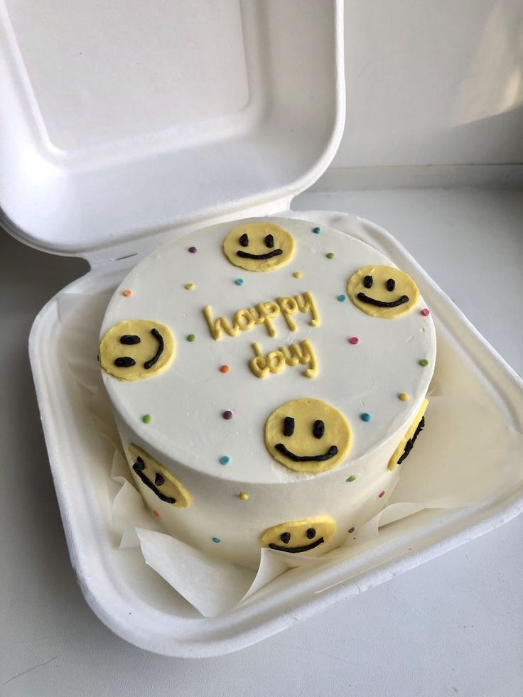 a white cake with yellow smiley faces on it in a foam container that says happy day