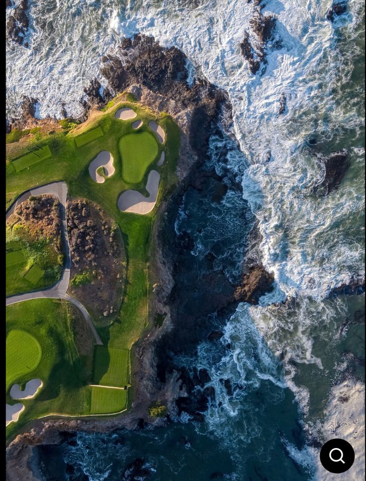 an aerial view of a golf course on the ocean with waves crashing in front of it