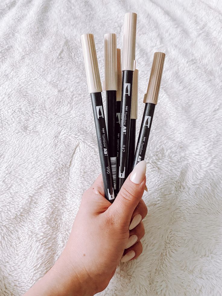 a person holding four pens in their hand on top of a white sheeted surface