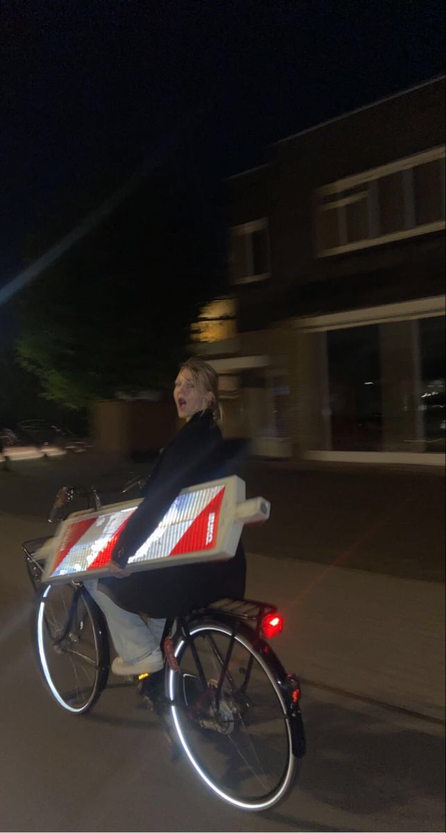 a woman is riding her bike down the street at night with red and white lights