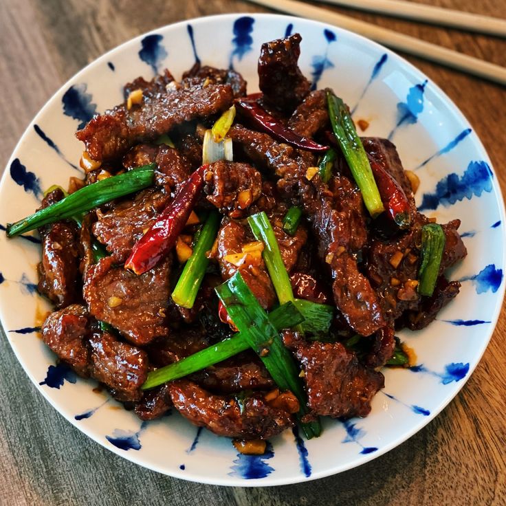 a white plate topped with meat and veggies next to two chopsticks