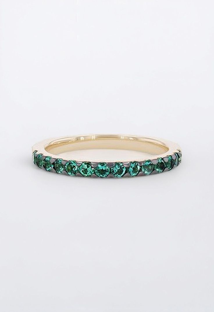 a gold band with green stones on the inside and outside, set against a white background