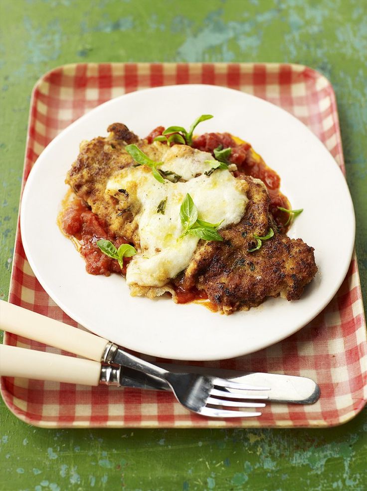 a white plate topped with meat covered in sauce and cheese on top of a checkered cloth