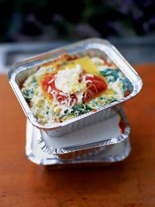 an aluminum container filled with lasagna casserole on top of a wooden table