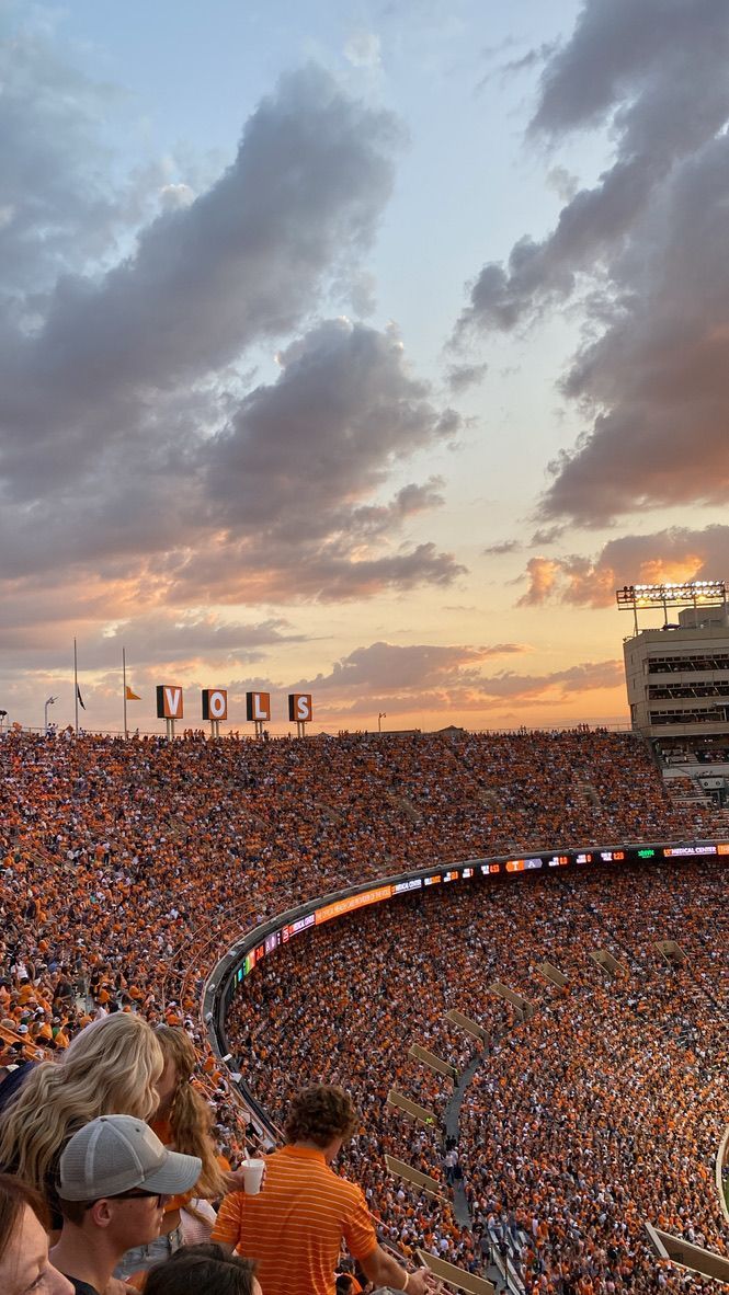 a large stadium filled with lots of people sitting on the bleachers at sunset