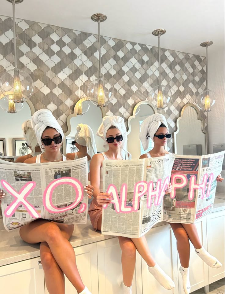 three women sitting on a counter with towels over their heads and reading the paper xo