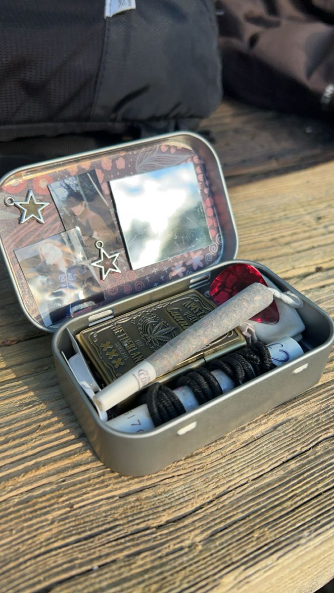 an open tin with some items in it on a wooden table next to a backpack