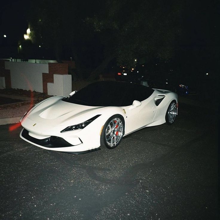 a white sports car parked on the side of the road at night with its lights on