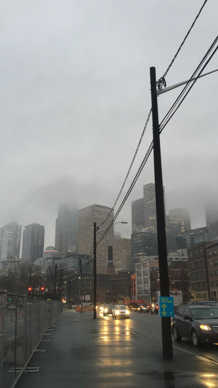 cars are driving down the street in front of tall buildings on a rainy day with fog