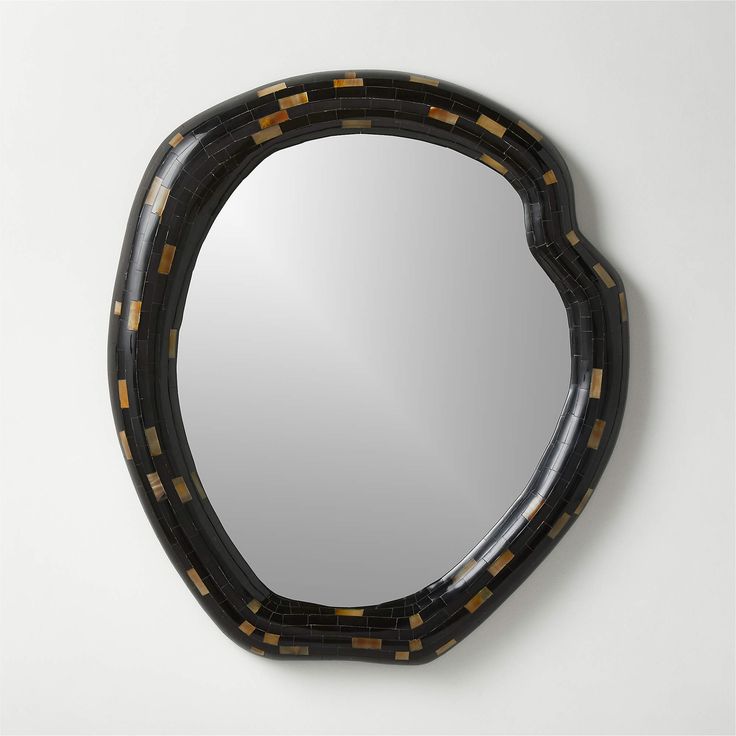 an oval mirror with black and gold designs on the edges, hanging on a wall