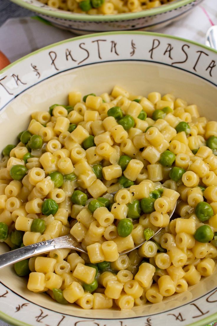 a bowl filled with pasta and peas on top of a table next to another bowl