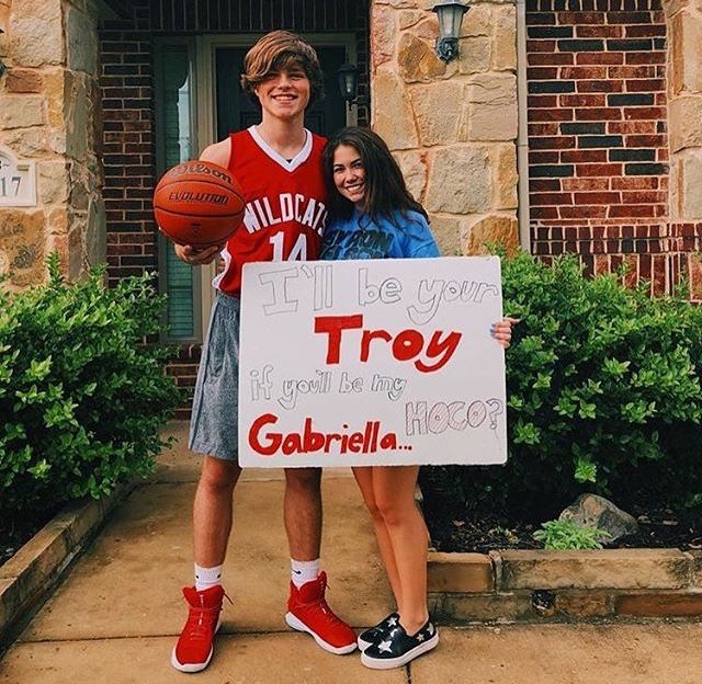 two people holding a sign in front of a brick building that says, i'll be your troy