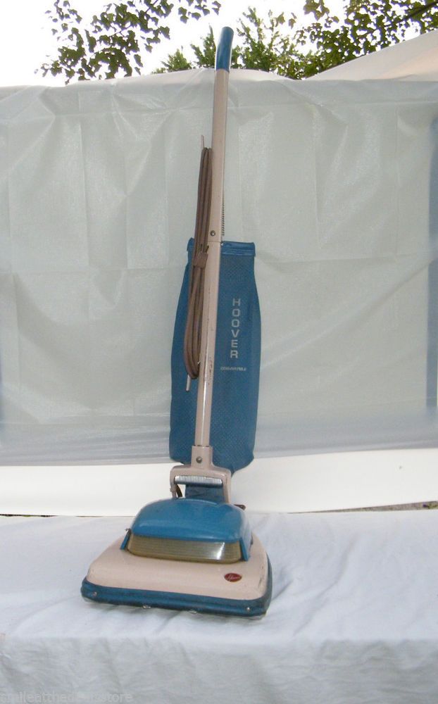 a blue and beige vacuum on top of a white sheet covered bed with trees in the background